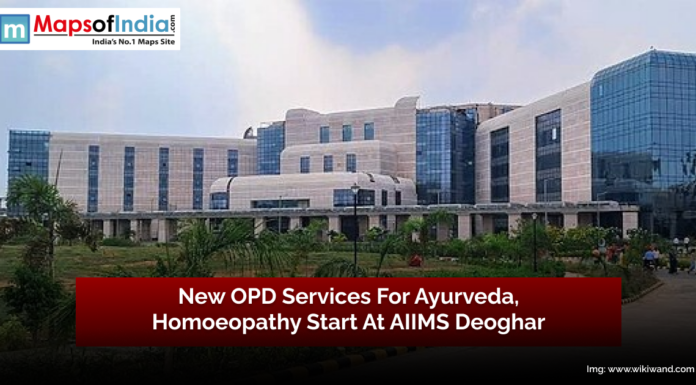 New OPD Services for Ayurveda, Homeopathy Start at AIIMS Deoghar A modern multi-story hospital building with large glass windows and a landscaped garden in front. Overlay text in a red banner reads, "New OPD Services For Ayurveda, Homoeopathy Start At AIIMS Deoghar."