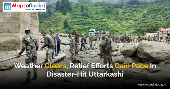 Indian Army personnel engaged in relief and rescue operations amid cleared weather in disaster-hit Uttarkashi, with damaged terrain and buildings in the background.