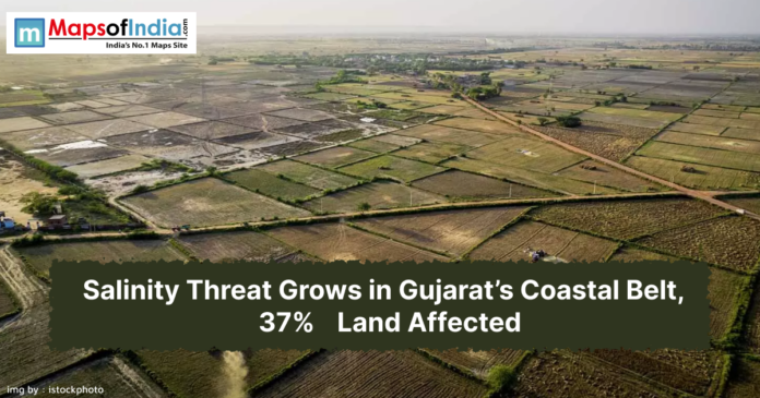An aerial photograph shows a vast expanse of agricultural fields. Many of the fields appear dry and are divided into square and rectangular plots by earthen boundaries and small roads. Some fields are barren, while others have some vegetation.
