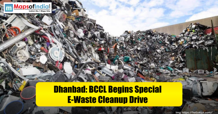 A large pile of discarded electronic waste including cables, wires, and old appliances is shown in Dhanbad. The image highlights a cleanup drive launched by BCCL to manage and recycle e-waste, with a Maps of India logo and the caption “Dhanbad: BCCL Begins Special E-Waste Cleanup Drive” displayed on a yellow banner.
