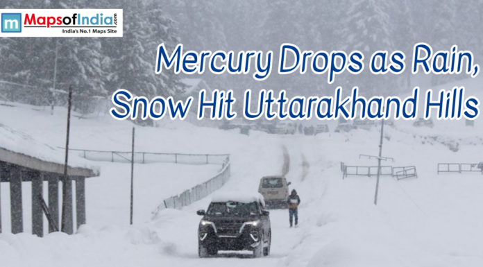 Mercury Drops as Rain, Snow Hit Uttarakhand Hills Snow-covered road in the hills of Uttarakhand with vehicles and people navigating through heavy snowfall. The headline reads, “Mercury Drops as Rain, Snow Hit Uttarakhand Hills,” with the Maps of India logo in the corner.