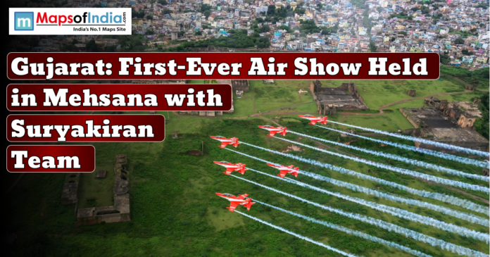 An aircraft formation flying in the sky during Gujarat's first-ever air show held in Mehsana with Suryakiran Team, with a lush green landscape and historic structures below.