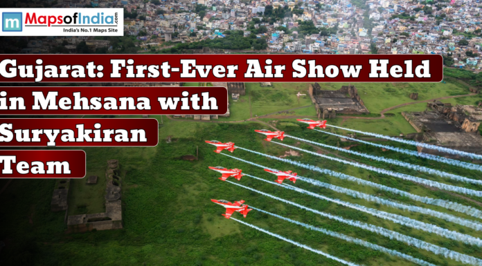 Gujarat: First-Ever Air Show Held in Mehsana with Suryakiran Team An aircraft formation flying in the sky during Gujarat's first-ever air show held in Mehsana with Suryakiran Team, with a lush green landscape and historic structures below.