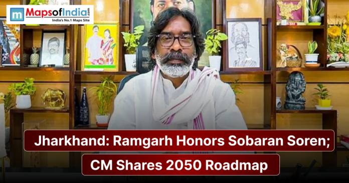 A man in traditional white attire sits before a decorated shelf with portraits, alongside a banner reading “Jharkhand: Ramgarh Honors Sobaran Soren; CM Shares 2050 Roadmap.”