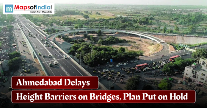 Ahmedabad Delays Aerial view of a busy Ahmedabad flyover and road junction with vehicles in motion, featuring a headline reading “Ahmedabad Delays Height Barriers on Bridges, Plan Put on Hold” and the Maps of India logo.