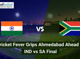 An aerial view of a packed cricket stadium at night under bright floodlights, divided into two halves featuring the national flags of India and South Africa. The text overlay reads, "Cricket Fever Grips Ahmedabad Ahead of IND vs SA Final."