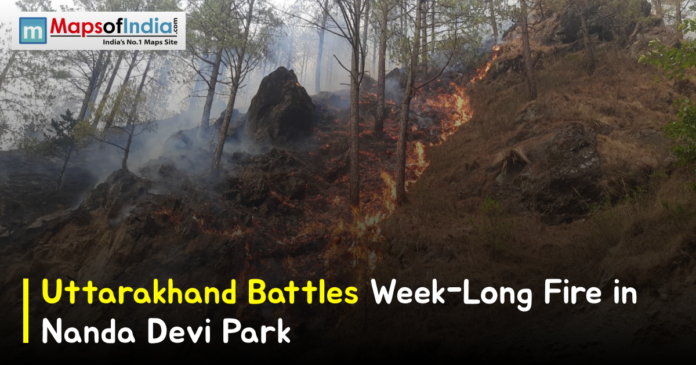 Forest fire burning on a hillside in Nanda Devi National Park, Uttarakhand, with flames and smoke spreading among trees, featuring the headline “Uttarakhand Battles Week-Long Fire in Nanda Devi Park.”