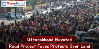 Uttarakhand Elevated Road Project Faces Protests Over Land Large crowd of protesters marching along a busy Uttarakhand street, holding placards and flags as traffic lines the road, highlighting opposition to the elevated road project over land acquisition.