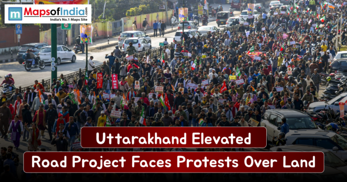Large crowd of protesters marching along a busy Uttarakhand street, holding placards and flags as traffic lines the road, highlighting opposition to the elevated road project over land acquisition.
