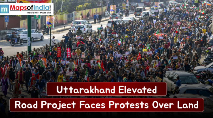 Uttarakhand Elevated Road Project Faces Protests Over Land Large crowd of protesters marching along a busy Uttarakhand street, holding placards and flags as traffic lines the road, highlighting opposition to the elevated road project over land acquisition.