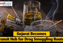 Gujarat Becomes Transit Hub for Drug Smuggling Routes Still life showing syringes, pills, a cigarette in an ashtray, and a glass of liquid on a wooden table as a headline reports Gujarat becoming a transit hub for drug smuggling routes.