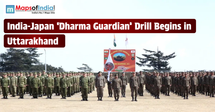 A group of Indian and Japanese soldiers standing in formation at an outdoor military grounds for the 'Dharma Guardian' joint exercise in Uttarakhand. A large banner and the national flags of India and Japan are visible in the background, with the Maps of India logo in the top left corner.