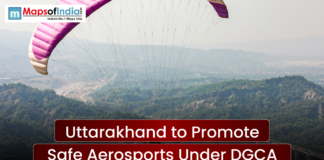 Uttarakhand to Promote Safe Aerosports Under DGCA A wide scenic shot of a person paragliding over a lush green mountainous valley under a clear sky. A text banner reads "Uttarakhand to Promote Safe Aerosports Under DGCA" with the Maps of India logo in the top left.